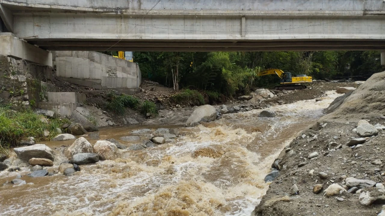 Corriente de agua entre bloques de roca bajo un puente de concreto.