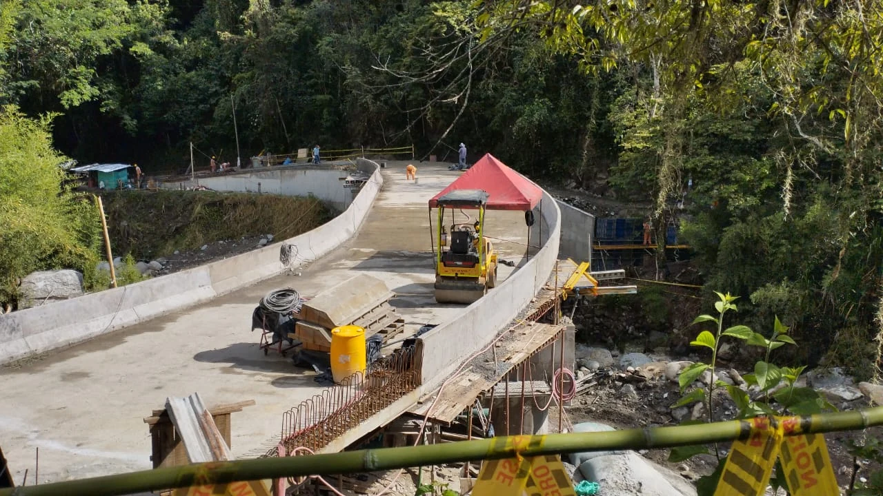 Puente en un entorno de obra con maquinaria, personas y vegetación alrededor.