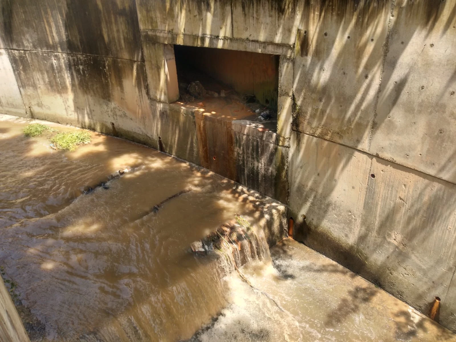 Agua que pasa sobre un desnivel en un canal de concreto, junto a una abertura lateral.