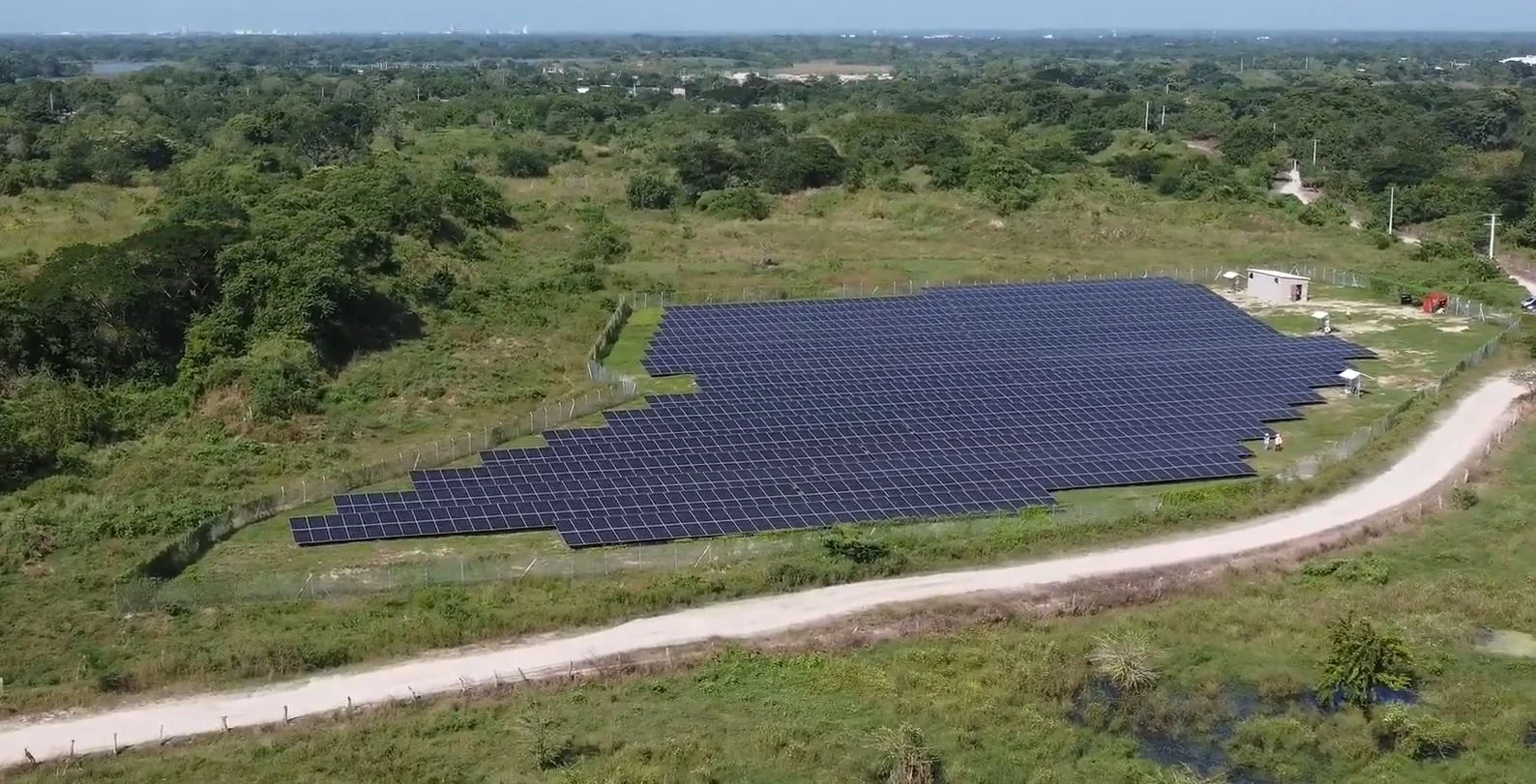 Vista aérea de un parque solar con paneles, una vía curva y vegetación alrededor.